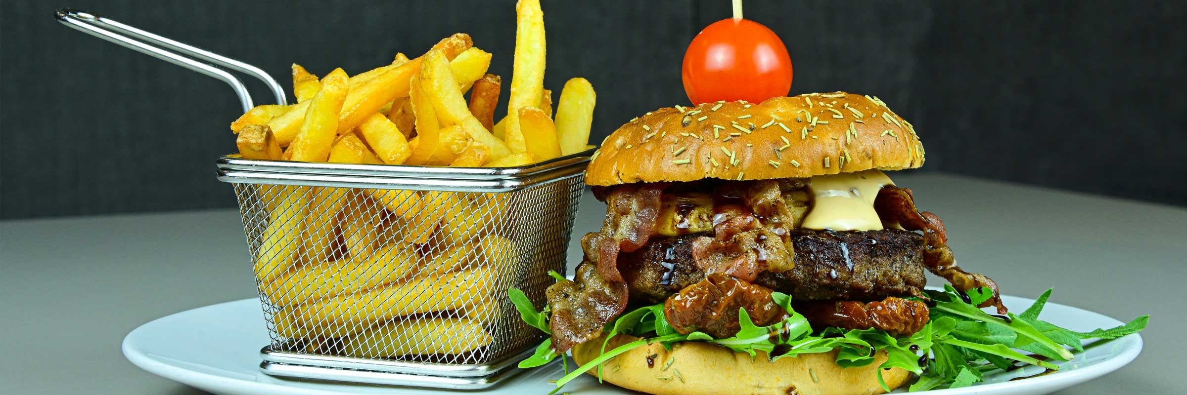 Luisenhof-Burger vom Angusrind, belegt mit Ziegenkäse, Bacon, getrockneten Tomaten und frischem Rucola, dazu Pommes frites